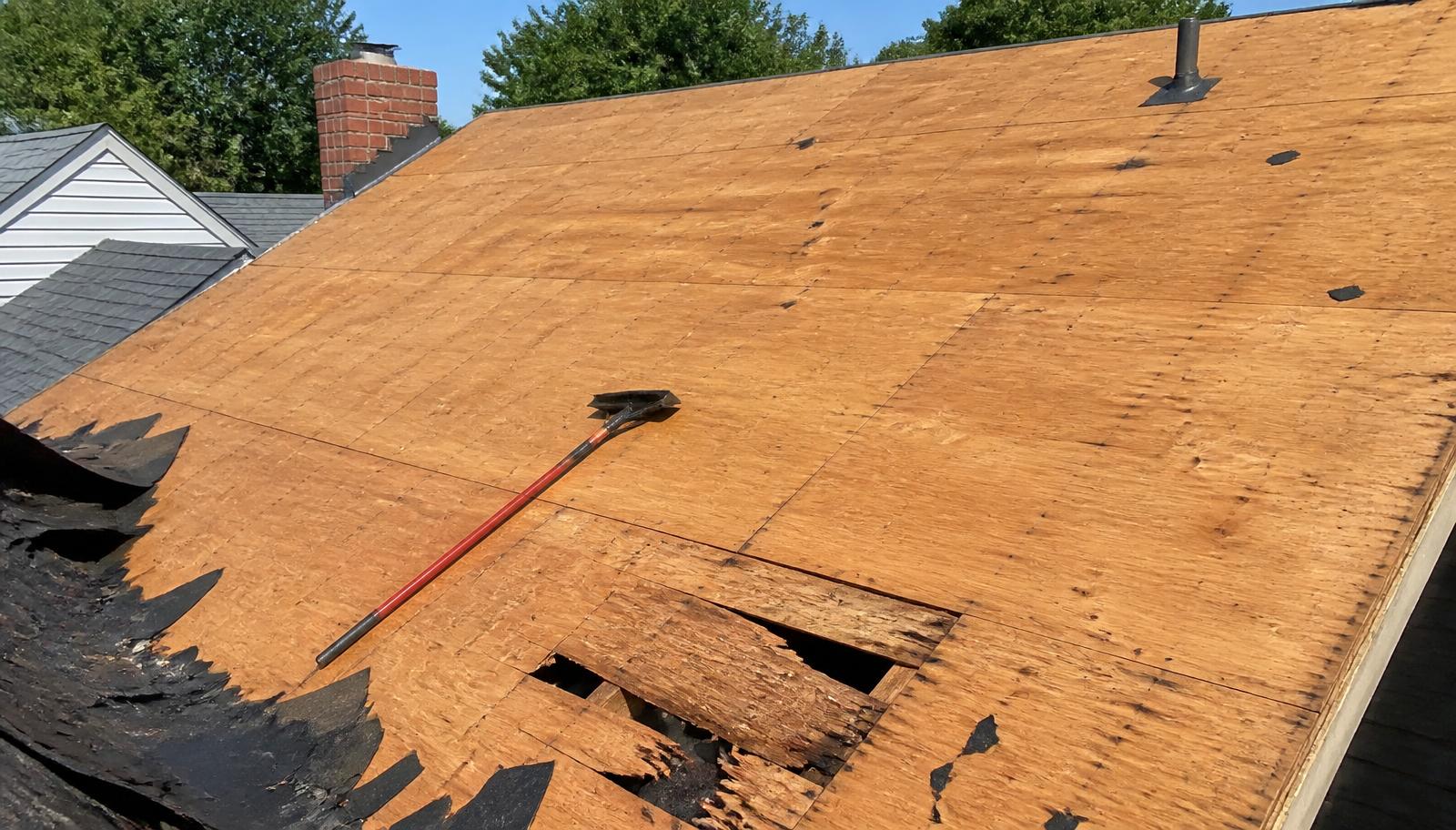 Roof tear-off in progress showing exposed plywood decking with damaged boards