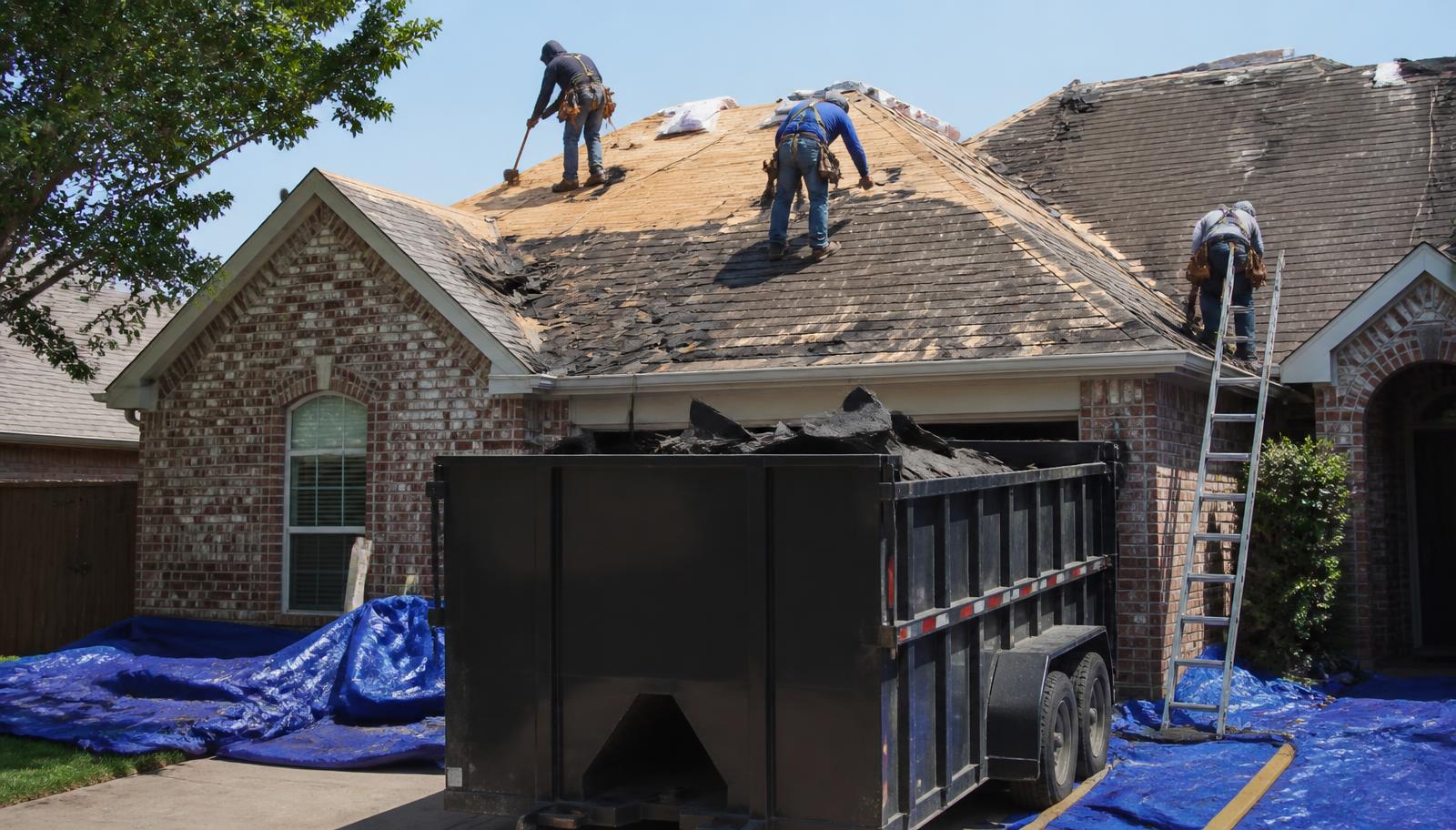 Roofing crew performing a shingle tear off on a brick home in North Texas with a dumpster in the driveway
